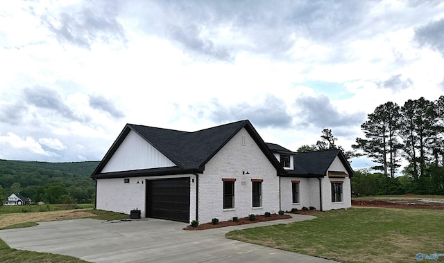 modern farmhouse featuring a front yard, a garage, a shingled roof, driveway, and brick siding