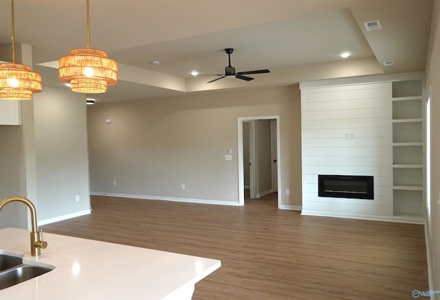 unfurnished living room featuring a raised ceiling, wood finished floors, recessed lighting, and a sink