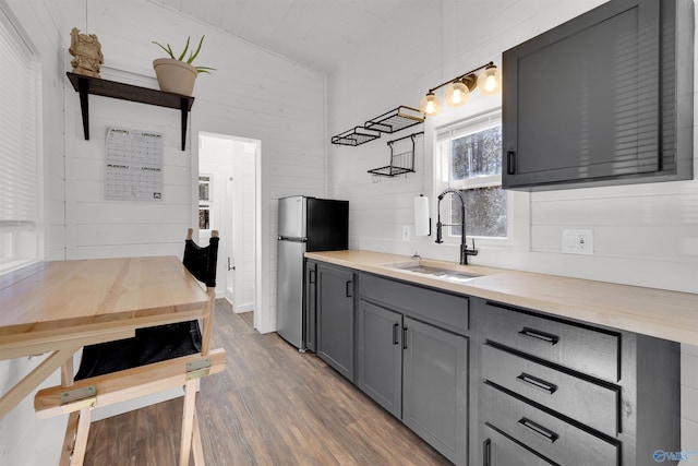 kitchen featuring wood walls, sink, hardwood / wood-style flooring, butcher block counters, and stainless steel refrigerator