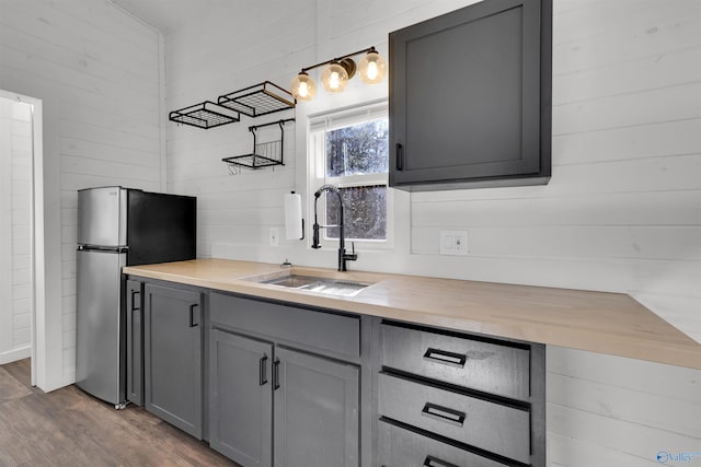 kitchen featuring gray cabinetry, sink, butcher block countertops, wood walls, and hardwood / wood-style flooring