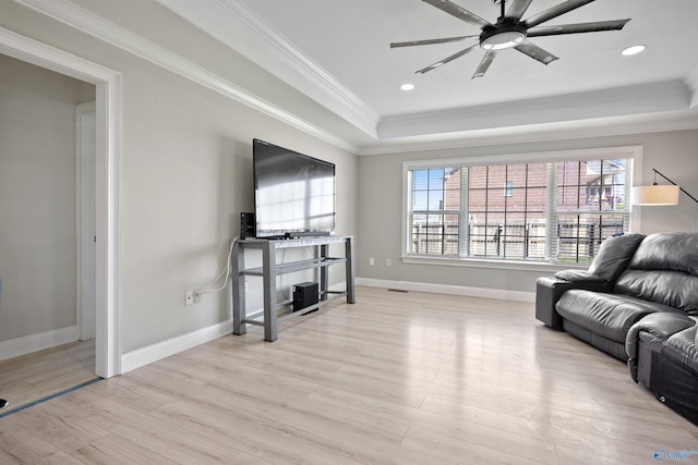 living room featuring light wood-style flooring, a tray ceiling, baseboards, a ceiling fan, and crown molding