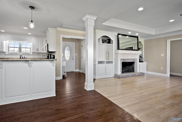 unfurnished living room featuring recessed lighting, dark wood-style floors, a raised ceiling, ornamental molding, and baseboards