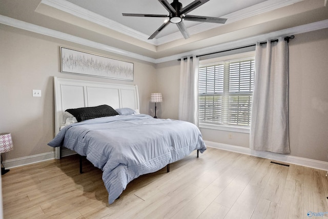 bedroom featuring light wood-style flooring, visible vents, baseboards, crown molding, and a raised ceiling
