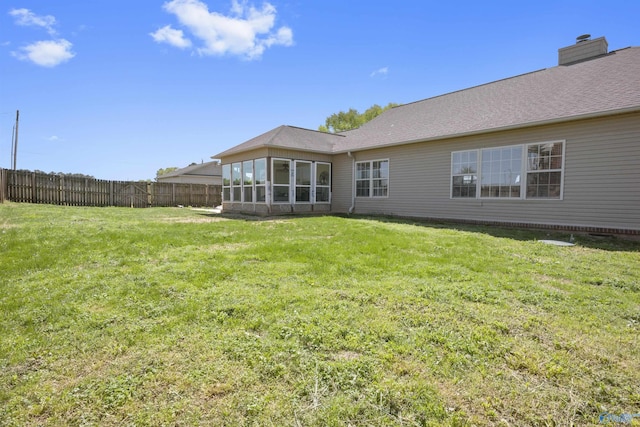 back of house featuring a chimney, fence, a shingled roof, a lawn, and a sunroom