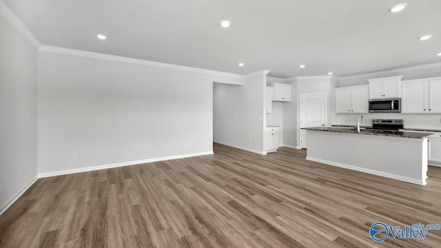 kitchen with white cabinetry, dark stone countertops, a kitchen island with sink, stainless steel appliances, and crown molding