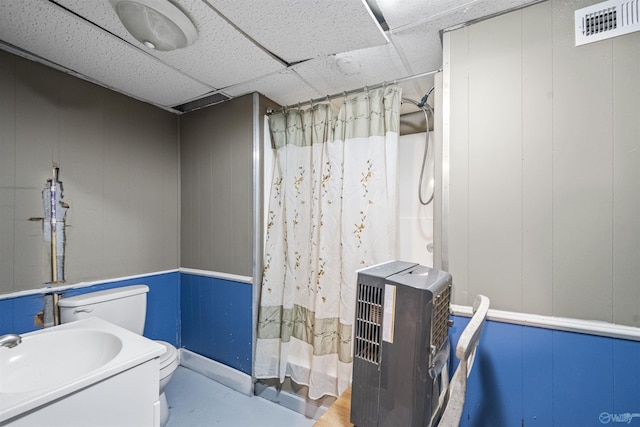 full bathroom featuring a shower with curtain, heating unit, toilet, a decorative wall, and a sink
