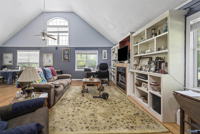 living area featuring wood finished floors, ceiling fan, a fireplace, and plenty of natural light