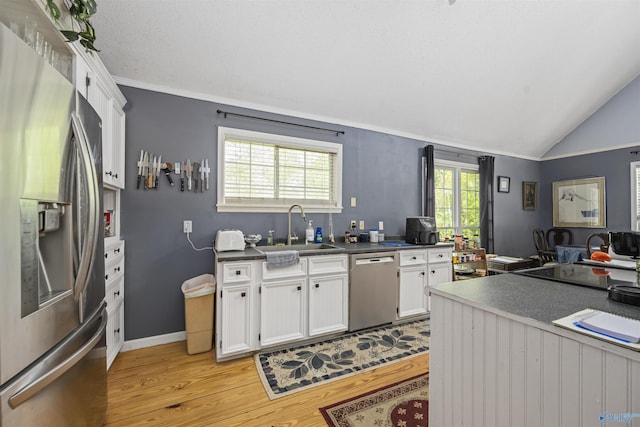 kitchen with appliances with stainless steel finishes, light wood finished floors, a sink, and dark countertops