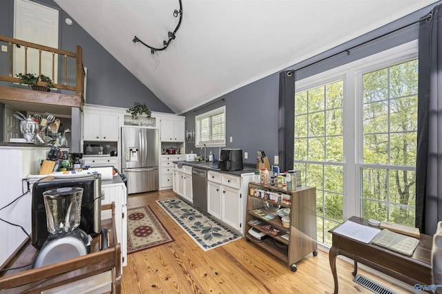 kitchen featuring light wood-type flooring, white cabinets, appliances with stainless steel finishes, and vaulted ceiling
