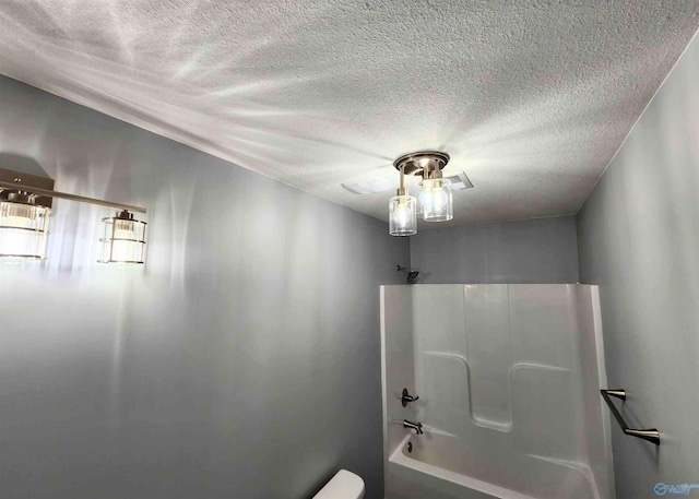 bathroom featuring shower / bathing tub combination, toilet, and a textured ceiling