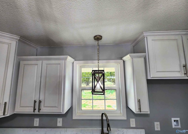 kitchen with white cabinetry, sink, hanging light fixtures, and a textured ceiling