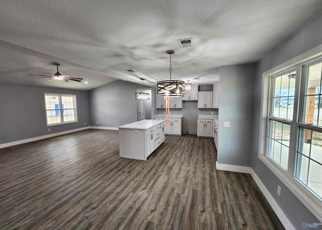 kitchen featuring dark wood-type flooring, white cabinetry, a center island, a textured ceiling, and pendant lighting