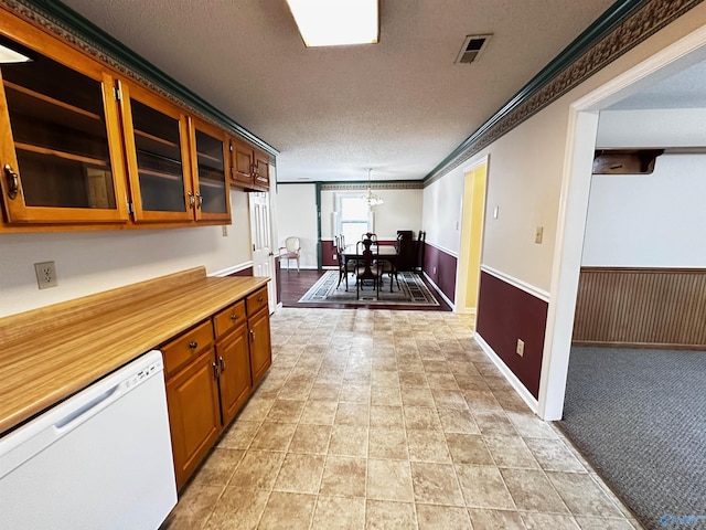 kitchen with a textured ceiling, a wainscoted wall, visible vents, dishwasher, and crown molding