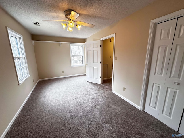 unfurnished bedroom with a textured ceiling, ceiling fan, visible vents, baseboards, and dark colored carpet