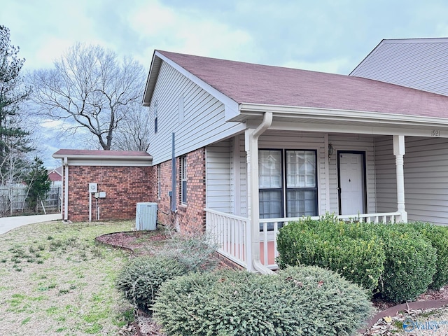 view of side of home with central air condition unit, roof with shingles, a porch, and brick siding