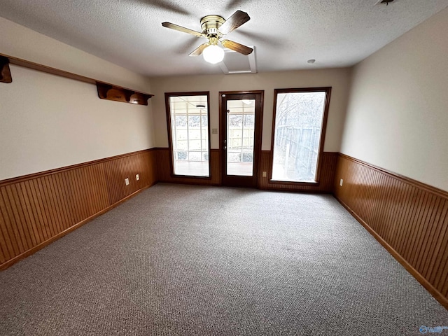 carpeted spare room with wooden walls, wainscoting, and a textured ceiling