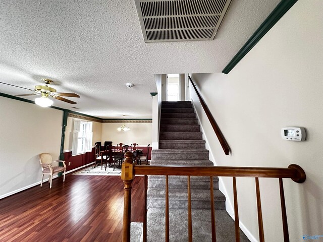 staircase featuring visible vents, a ceiling fan, a textured ceiling, wood finished floors, and baseboards