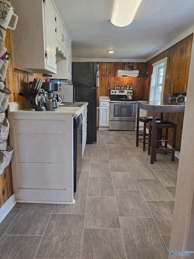 kitchen featuring wooden walls, light countertops, white cabinetry, under cabinet range hood, and black appliances