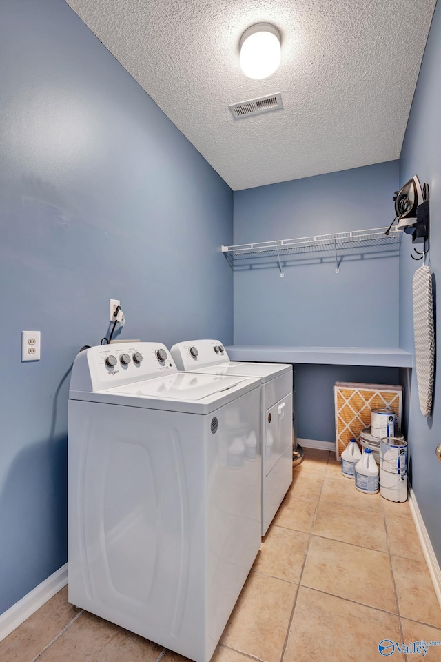 laundry area featuring light tile patterned flooring, washer and dryer, and a textured ceiling