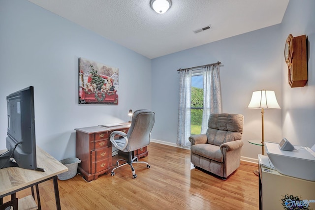 home office with a textured ceiling and light hardwood / wood-style flooring