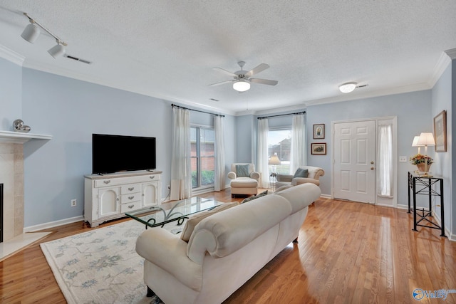 living room with track lighting, crown molding, ceiling fan, a fireplace, and a textured ceiling