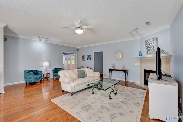 living room featuring ceiling fan, light hardwood / wood-style floors, ornamental molding, and a tiled fireplace