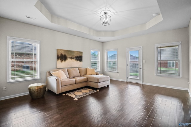 living area with dark wood-style floors, an inviting chandelier, a wealth of natural light, a tray ceiling, and visible vents