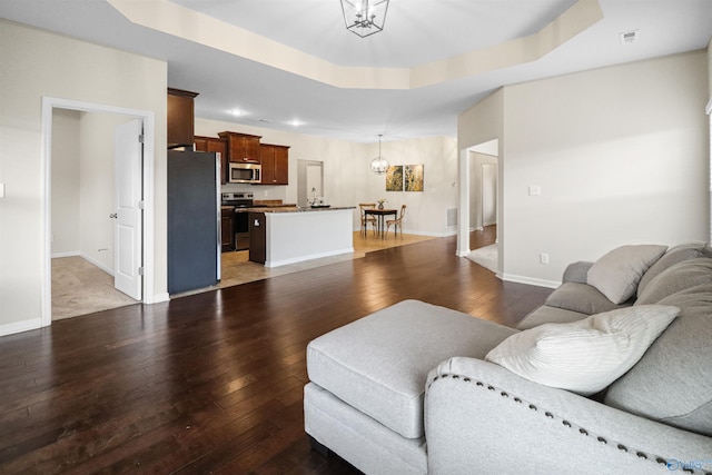 living room with visible vents, a raised ceiling, baseboards, wood-type flooring, and a notable chandelier