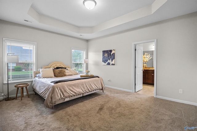 carpeted bedroom with baseboards, visible vents, a raised ceiling, and ensuite bath