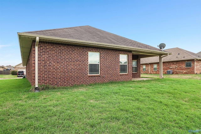 rear view of property featuring a lawn, roof with shingles, and brick siding