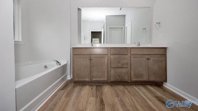 bathroom featuring a sink, wood finished floors, double vanity, baseboards, and a bath