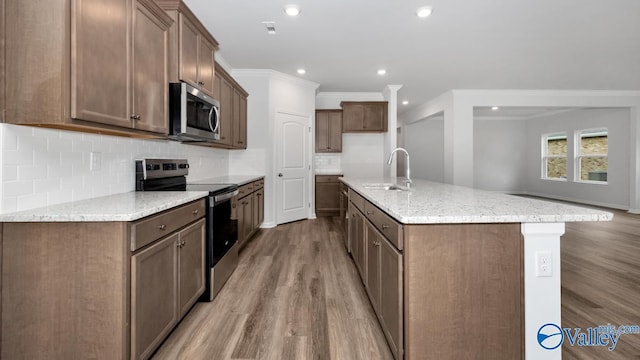 kitchen featuring ornamental molding, a sink, light wood-style floors, appliances with stainless steel finishes, and tasteful backsplash