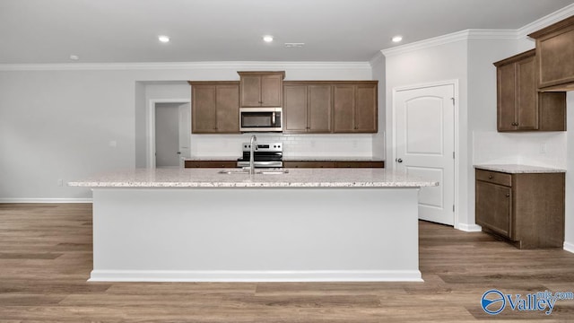 kitchen with a center island with sink, a sink, backsplash, wood finished floors, and appliances with stainless steel finishes