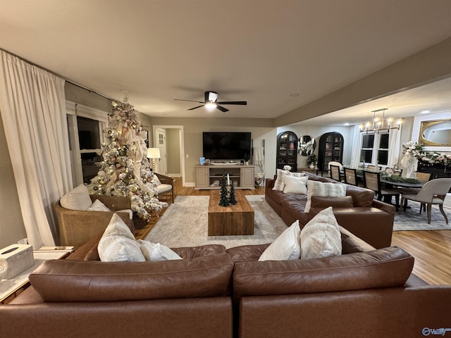 living room with ceiling fan with notable chandelier and light hardwood / wood-style flooring