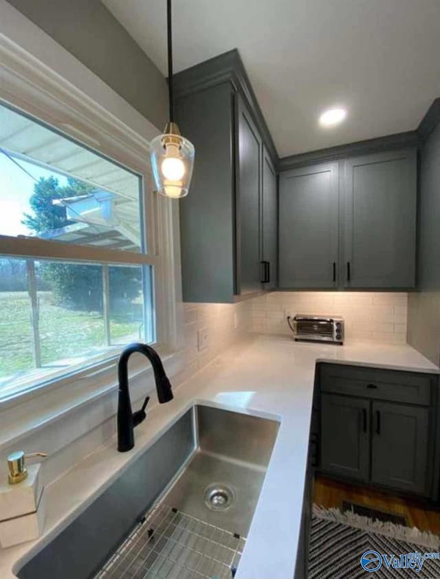 kitchen with pendant lighting, decorative backsplash, gray cabinetry, and sink