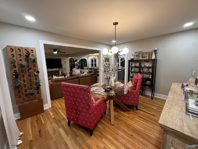 dining space featuring ceiling fan with notable chandelier and wood-type flooring