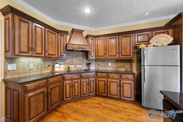 219 Sharp Dr, Gadsden, AL 35903 - kitchen featuring freestanding refrigerator, premium range hood, a textured ceiling, light wood-style floors, and brown cabinets