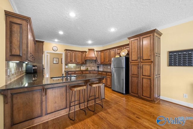 219 Sharp Dr, Gadsden, AL 35903 - kitchen featuring freestanding refrigerator, a peninsula, custom exhaust hood, wood finished floors, and ornamental molding