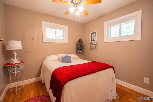 bedroom with baseboards, ceiling fan, wood finished floors, and electric panel