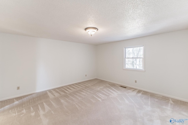 spare room featuring light carpet, visible vents, a textured ceiling, and baseboards