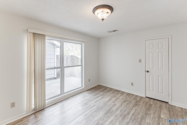 empty room featuring baseboards, wood finished floors, visible vents, and a textured ceiling