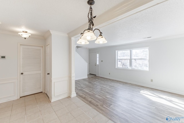 unfurnished dining area with visible vents, crown molding, light wood-style flooring, a decorative wall, and a textured ceiling