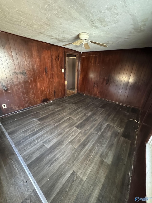 unfurnished bedroom with ceiling fan, dark hardwood / wood-style floors, a textured ceiling, and wood walls