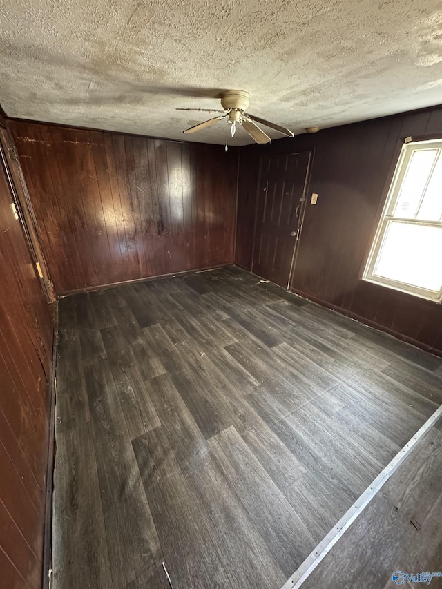 unfurnished room with ceiling fan, dark wood-type flooring, a textured ceiling, and wood walls