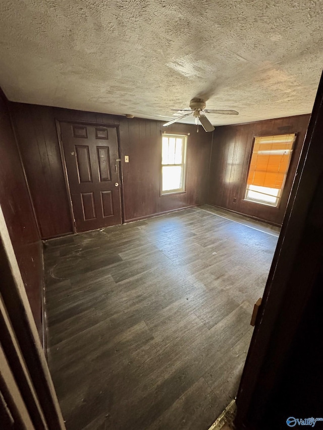 empty room featuring dark wood-type flooring, ceiling fan, wooden walls, and a textured ceiling