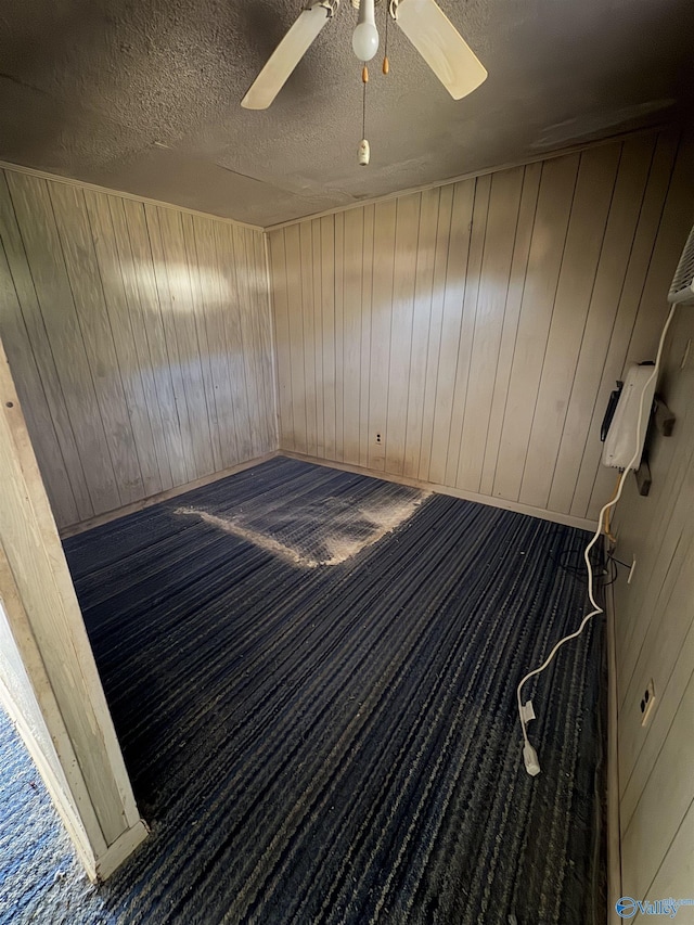 empty room featuring ceiling fan, a textured ceiling, and wooden walls