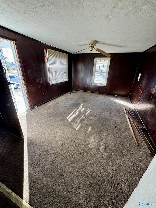 interior space with ceiling fan, carpet, a textured ceiling, and wood walls