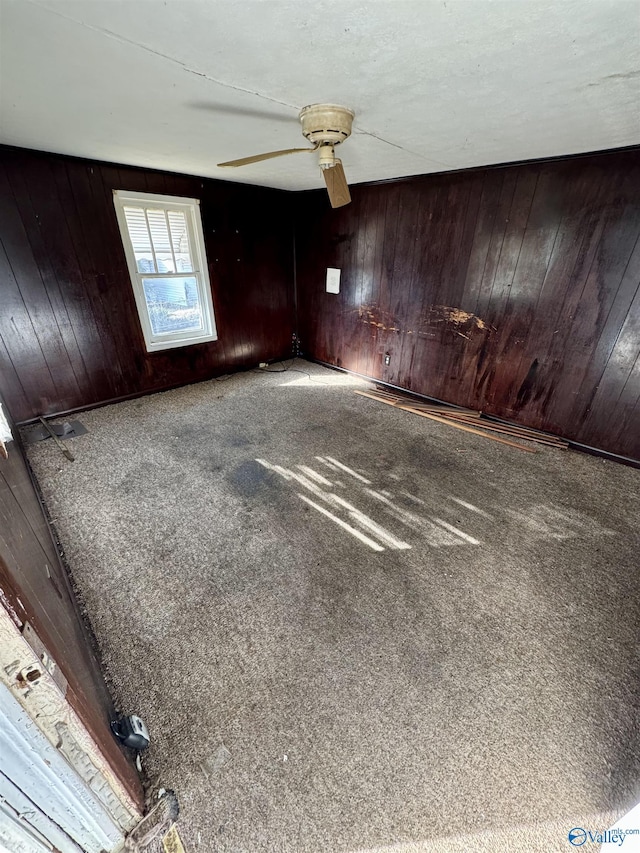 unfurnished room with ceiling fan, carpet floors, and wood walls