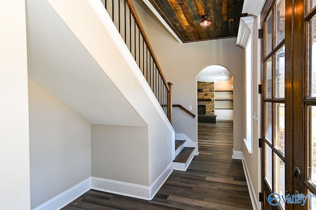 foyer entrance with dark wood-style floors, arched walkways, a stone fireplace, and baseboards