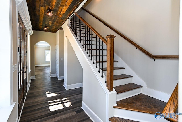 stairs with wooden ceiling, baseboards, arched walkways, and wood finished floors